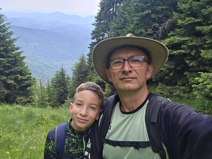 Alin și fiul său într-o drumeție, cu peisaj montan în fundal